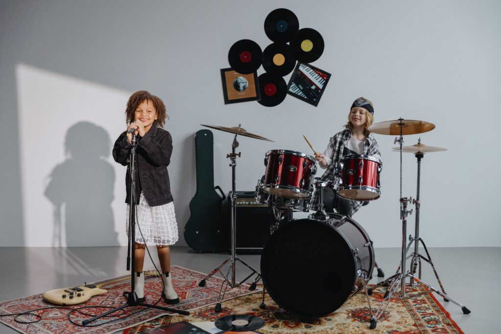 Children singing and drumming joyfully in a music studio with instruments.